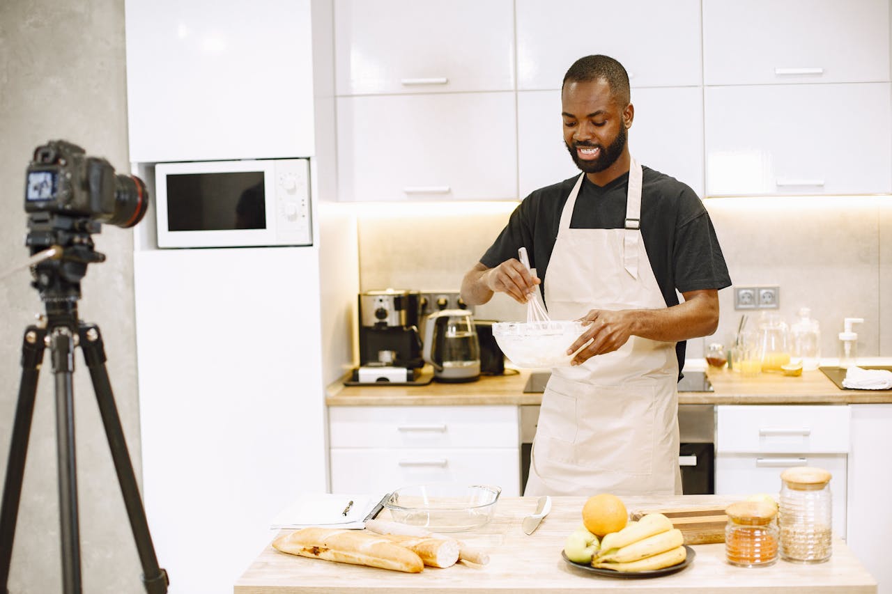 services-03 African American man cooking in kitchen for a vlogging session, recorded with DSLR camera.
