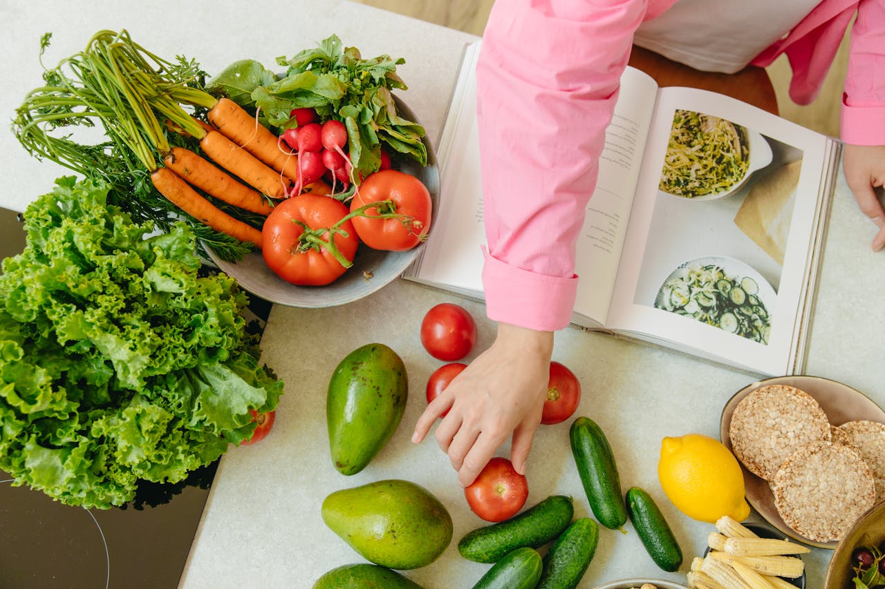 who-we-are Top view of fresh vegetables and hands arranging them with a recipe book, promoting healthy eating.